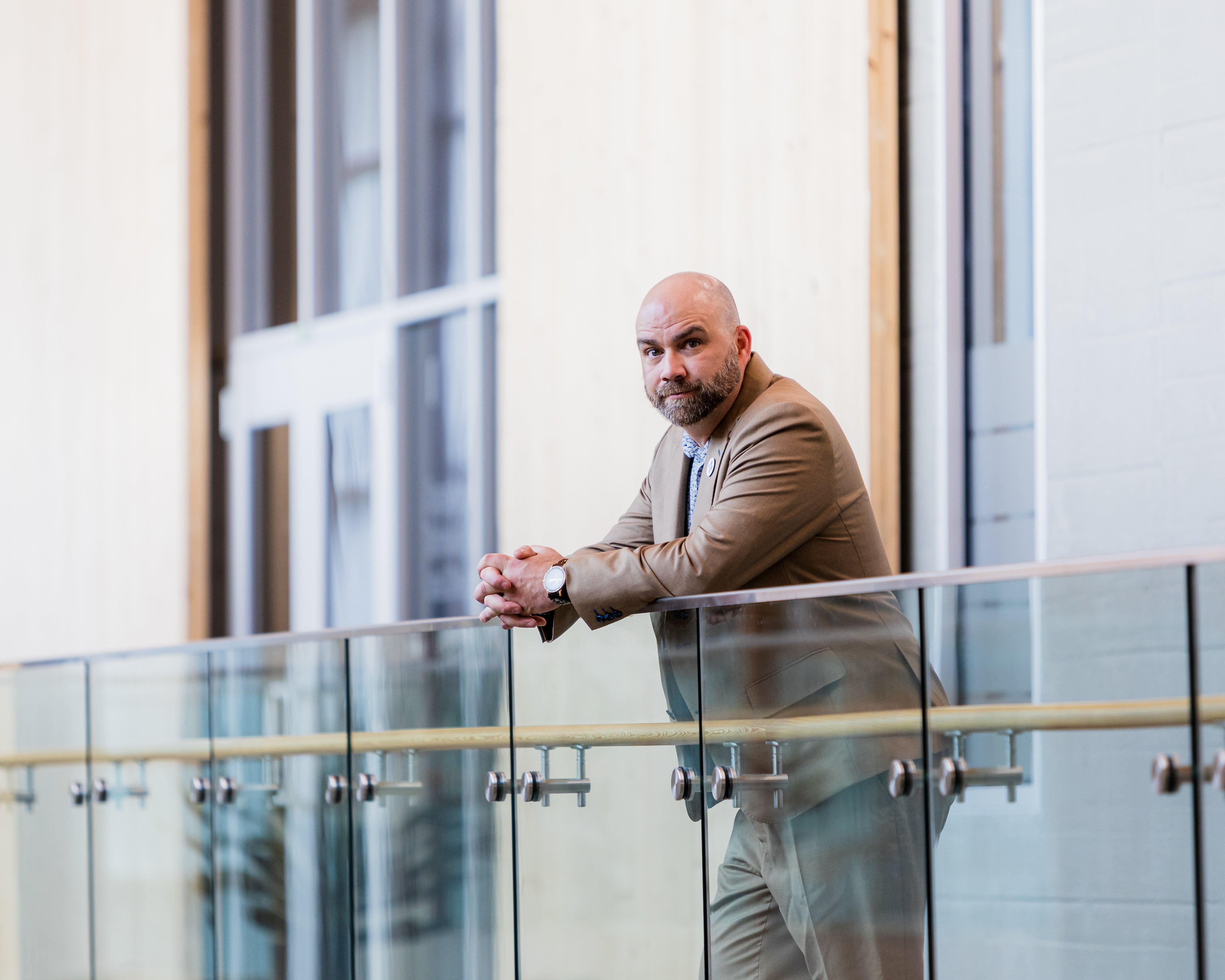 Man standing against a railing in a tan suit