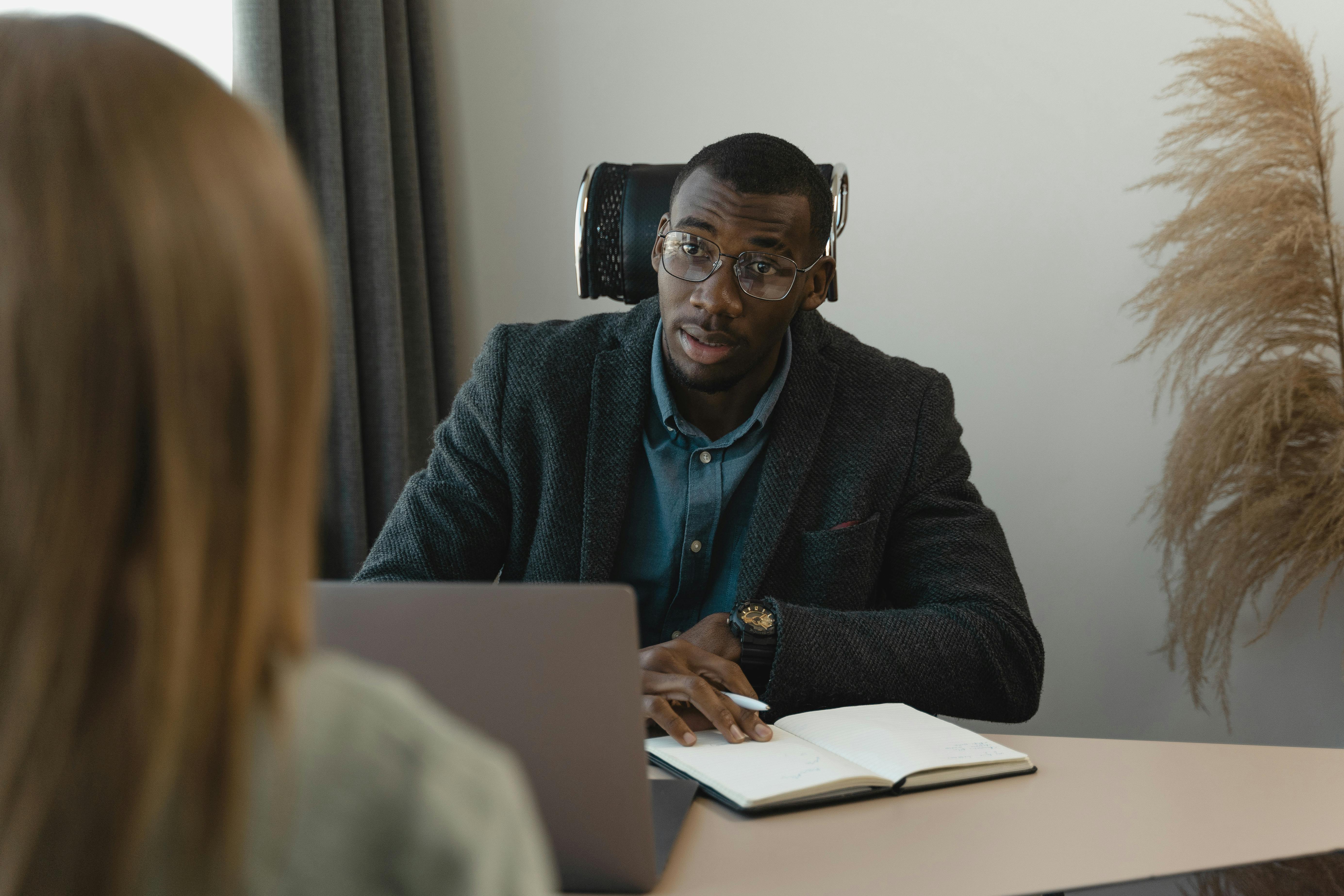 Manager and employee in a 1:1 meeting in a professional office setting, with a manager listening intently to employee feedback and taking notes.&nbsp;