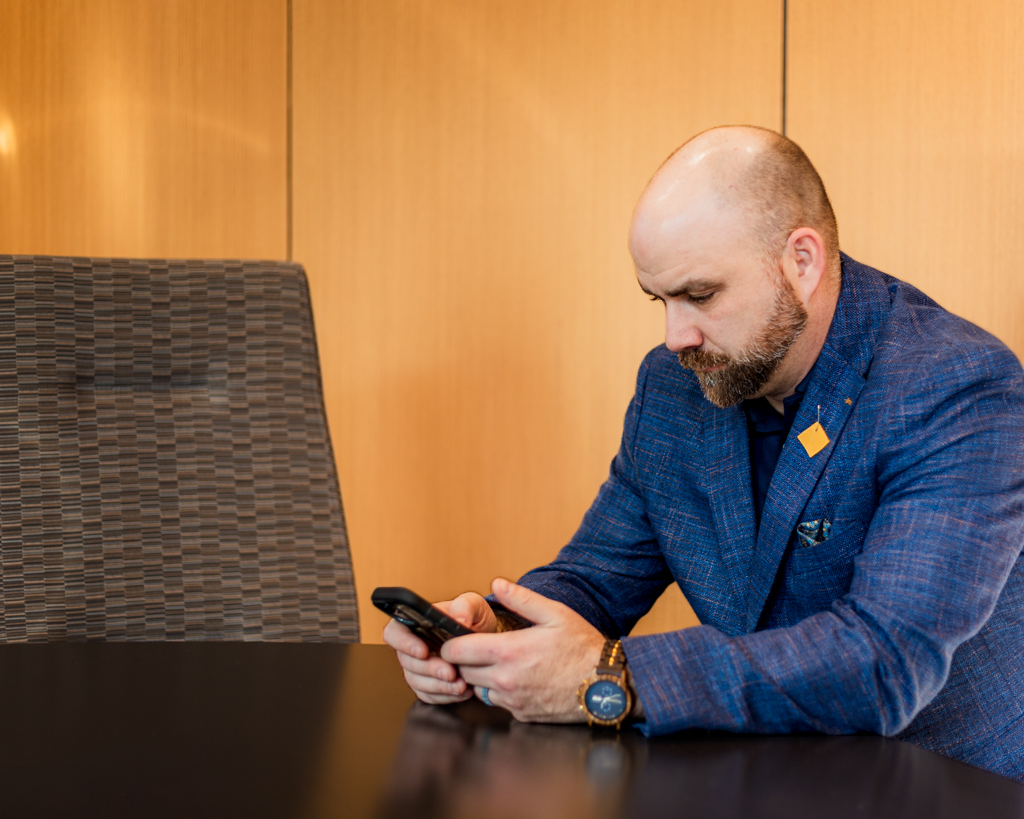 Man looking at his phone seated at a boardroom table